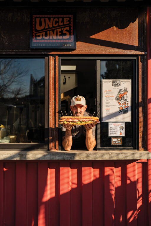 Man holding a sub sandwich in the pickup window of Uncle June's