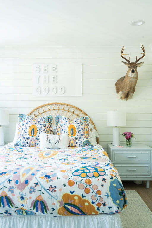 Girl's bedroom with white shiplap walls, colorful bed duvet and a deer's head hanging on the wall