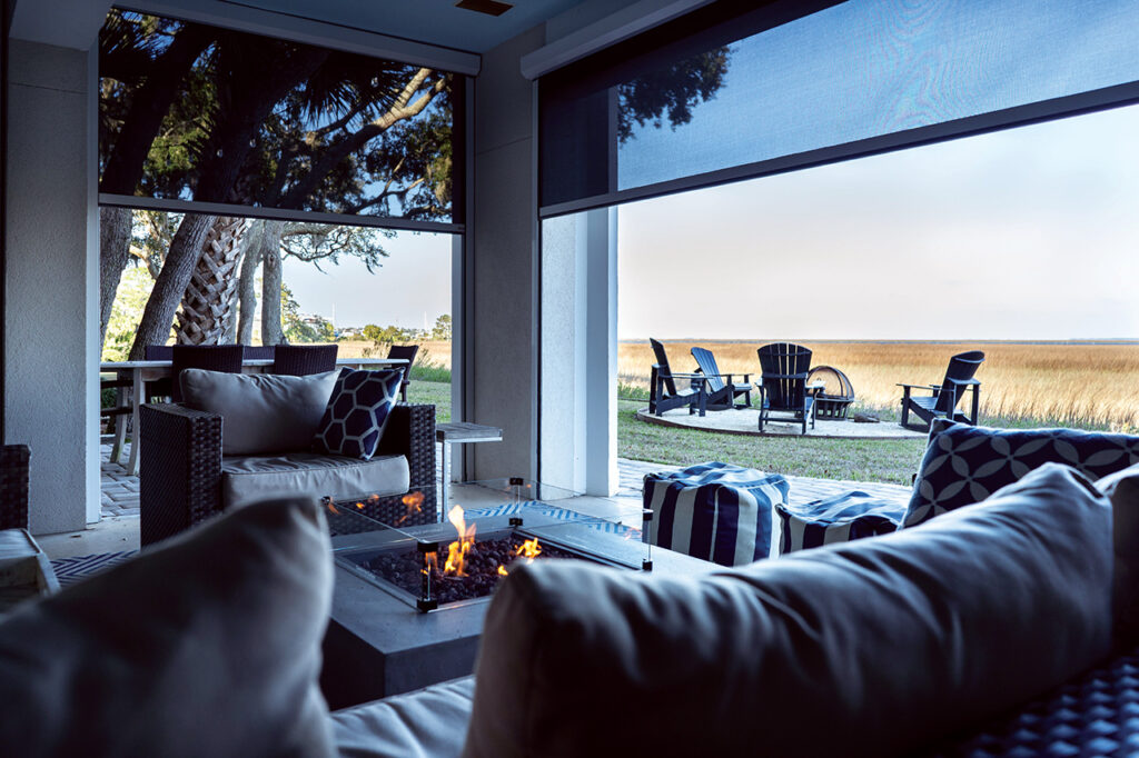 Screened-in patio with outdoor dining and lounging areas, and fire pit with a marsh view