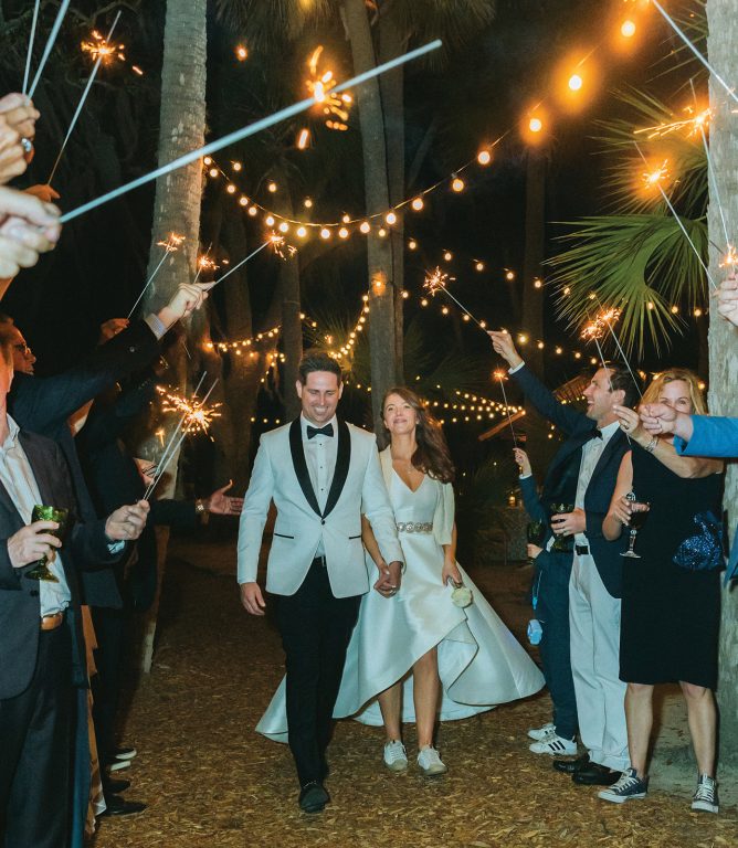 A bride and groom walking through a crowd of guests holding sparklers