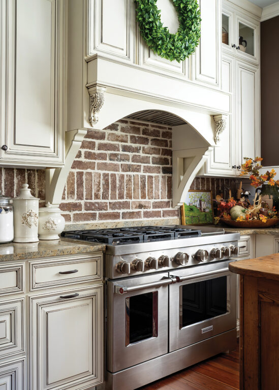 A kitchen with a stainless steal chef's oven, white cabinets and a brick backsplash