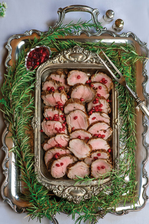 A silver platter with roasted pork tenderloin and fresh rosemary garnish