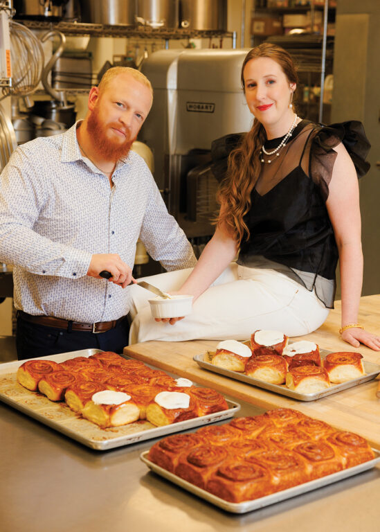 A man and woman putting frosting on cinnamon rolls