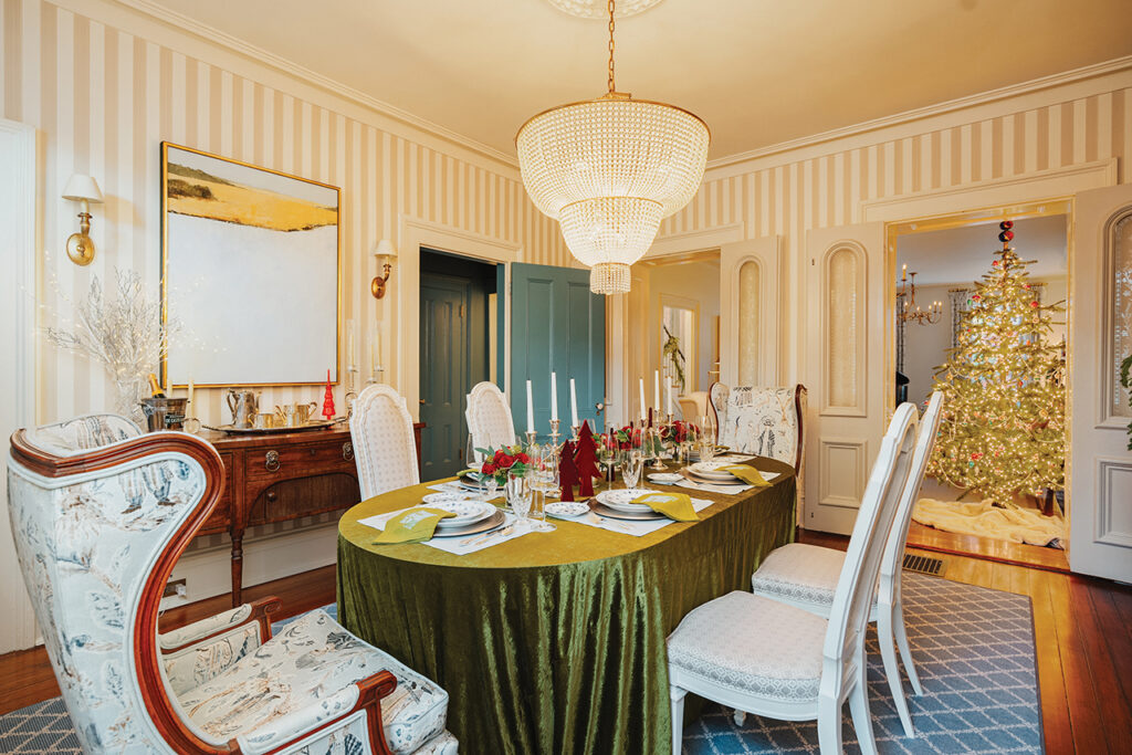 A dining room with vertical striped wallpaper and a green velvet tablecloth