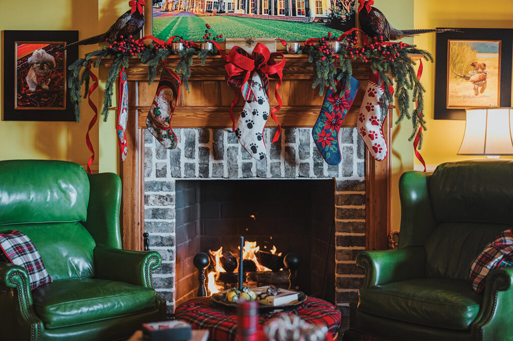 A fireplace flanked by two green leather armchairs and decorated with Christmas stockings
