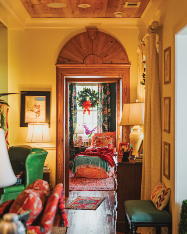 An entryway with yellow walls and a heart pine arch over the doorway leading int a sitting room with a chaise lounge