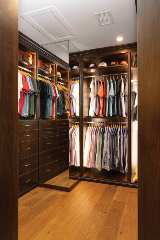 a walk-in closet with wood flooring and dark brown wood shelves and cabinets