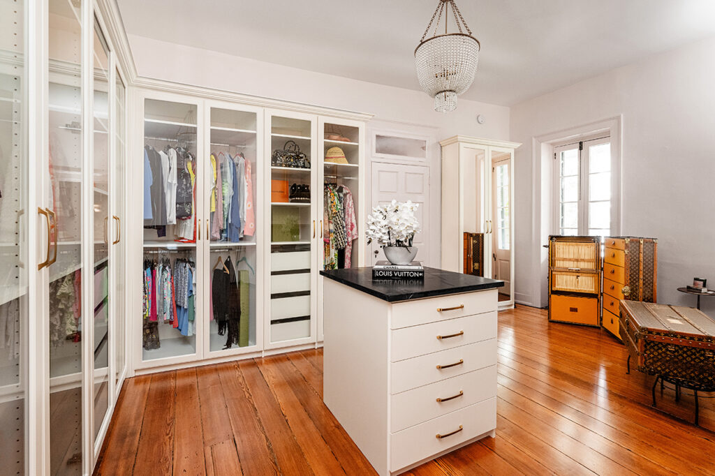 a closet suite with white floor-to-ceiling shelving and cabinetry, an island with white drawers and a black marble countertop, and wide-plank natural wood flooring