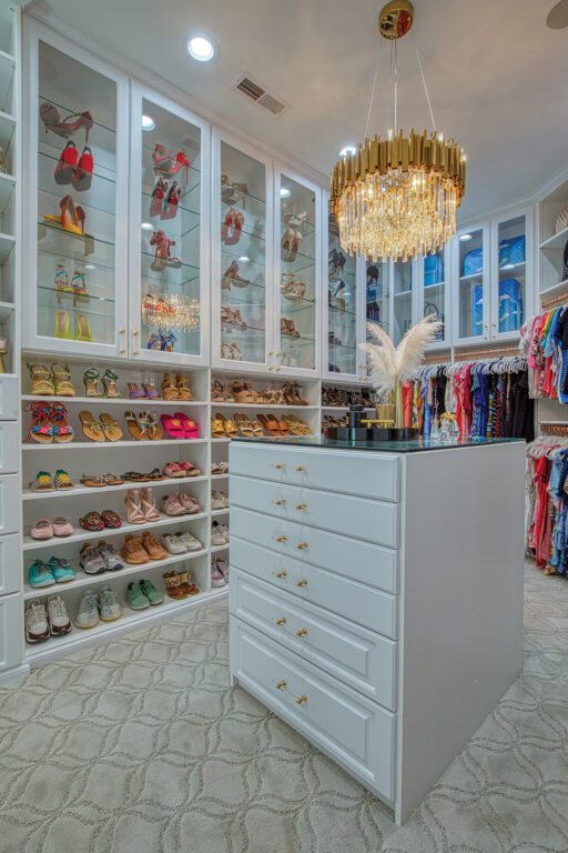 a closet suite with floor-to-ceiling shelves and cabinets, an island with drawers and a black marble countertop, and a gold chandelier