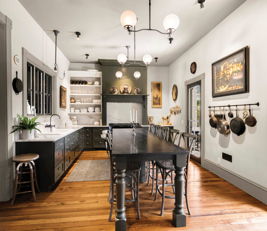 a kitchen with white walls, black cabinets, white open shelving, white marble countertops, and a long black wooden dining table