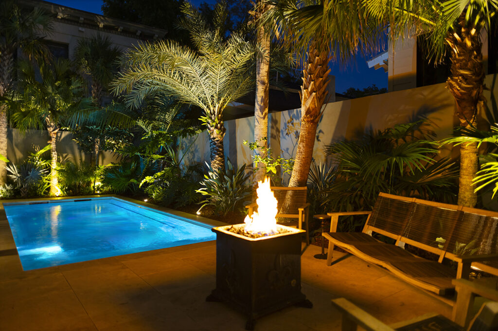 a small in-ground pool lit up at night next to a fire pit