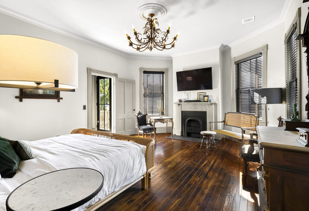 a bedroom with dark natural wood floor, fireplace, and white walls