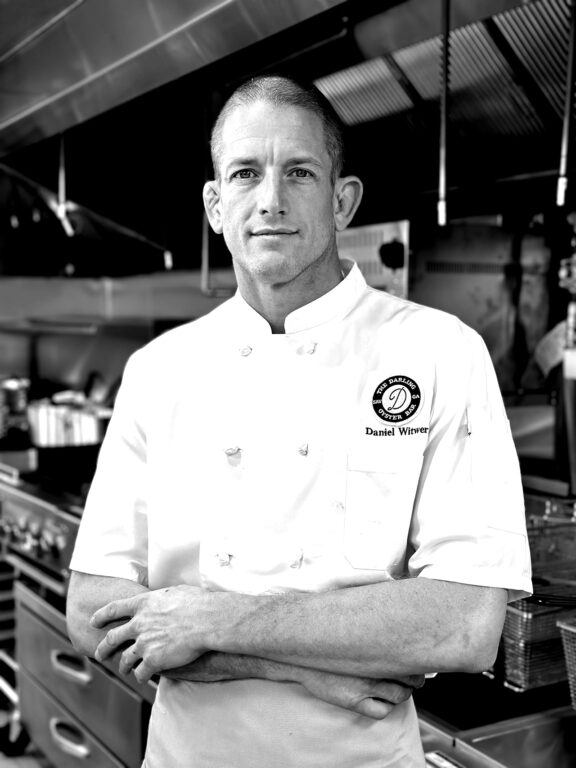 man in a chef coat standing with his arms crossed in front of his chest