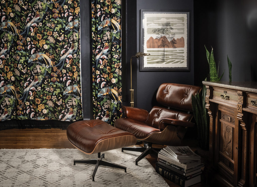 reading nook with dark leather chair, black walls, and dark bird-patterned curtains