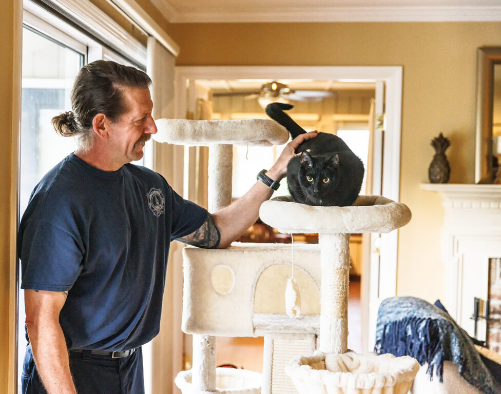 an off-duty firefighter petting a black cat in a cat tree