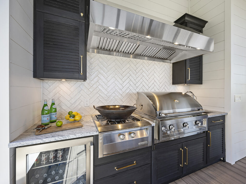 An outdoor kitchen with black cabinets a white herringbone subway tile backsplash, and grill