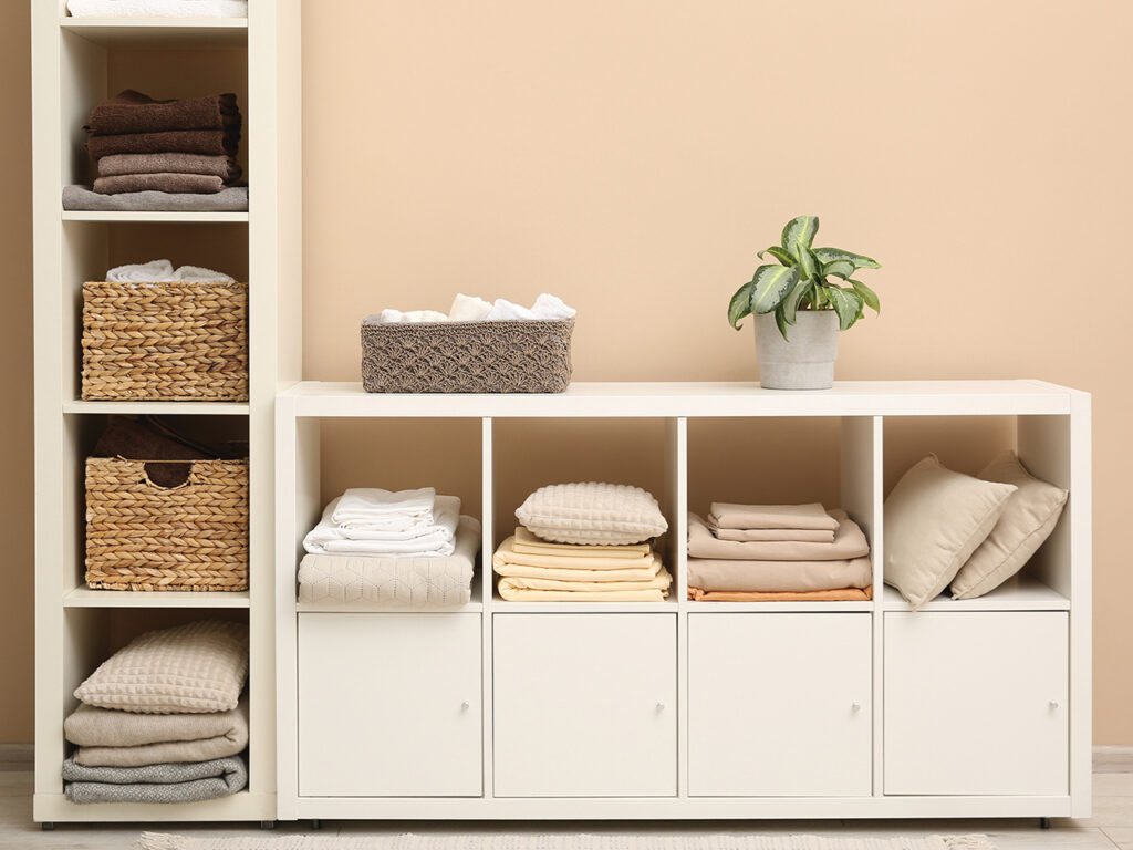 Folded linens, towels and pillows on shelving unit near beige wall.
