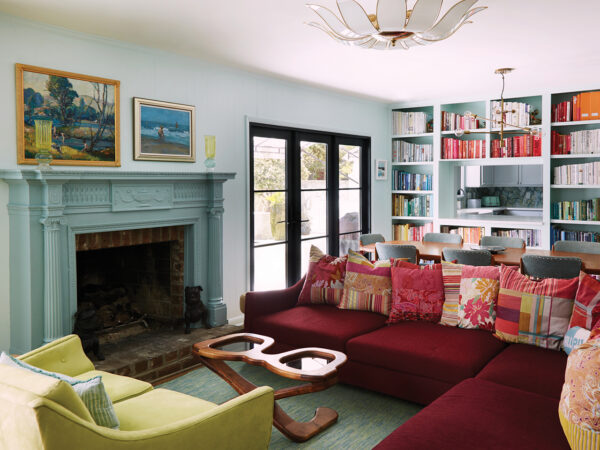 A vintage Bordeaux-red Roche Bobois sectional, chartreuse suede loveseat, hand-carved fireplace, and a coffee table shaped like sunglasses