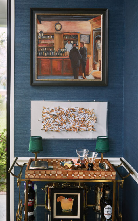 An artistic display of cigarette butts and a painting of a European bar scene above a brass bar cart
