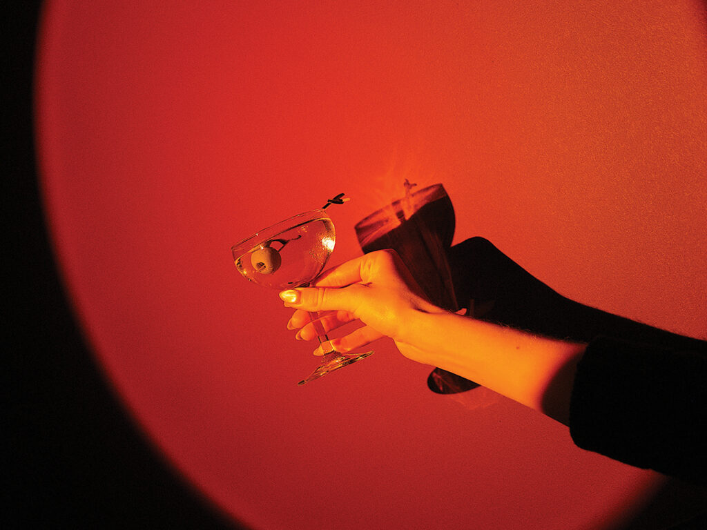 Woman's hand holding up a martini in front of a red wall