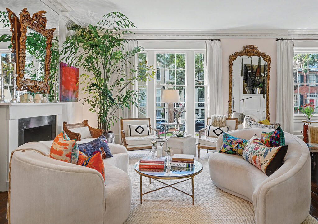 The living room with light beige sofas and rug, ornate gold-framed mirrors, and original dental molding