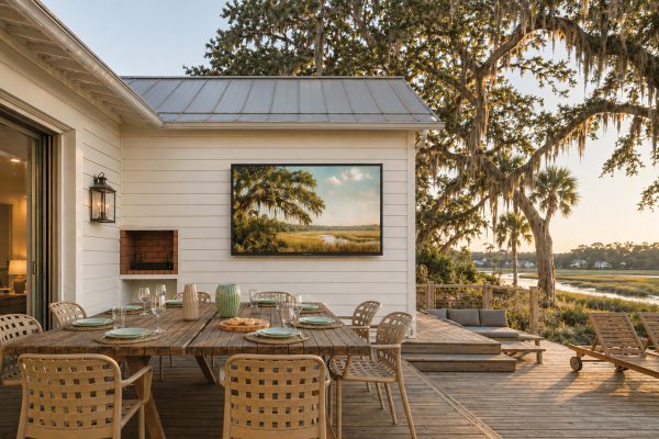 TV hanging on a wall next to an outdoor dining area on a deck on the marsh