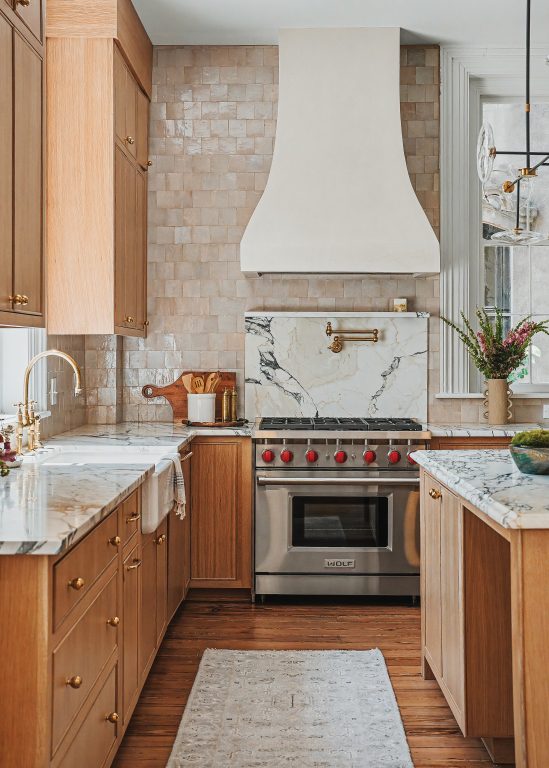 A kitchen with Italian marble countertops, Moroccan zellige backsplash, and an exposed brick fireplace